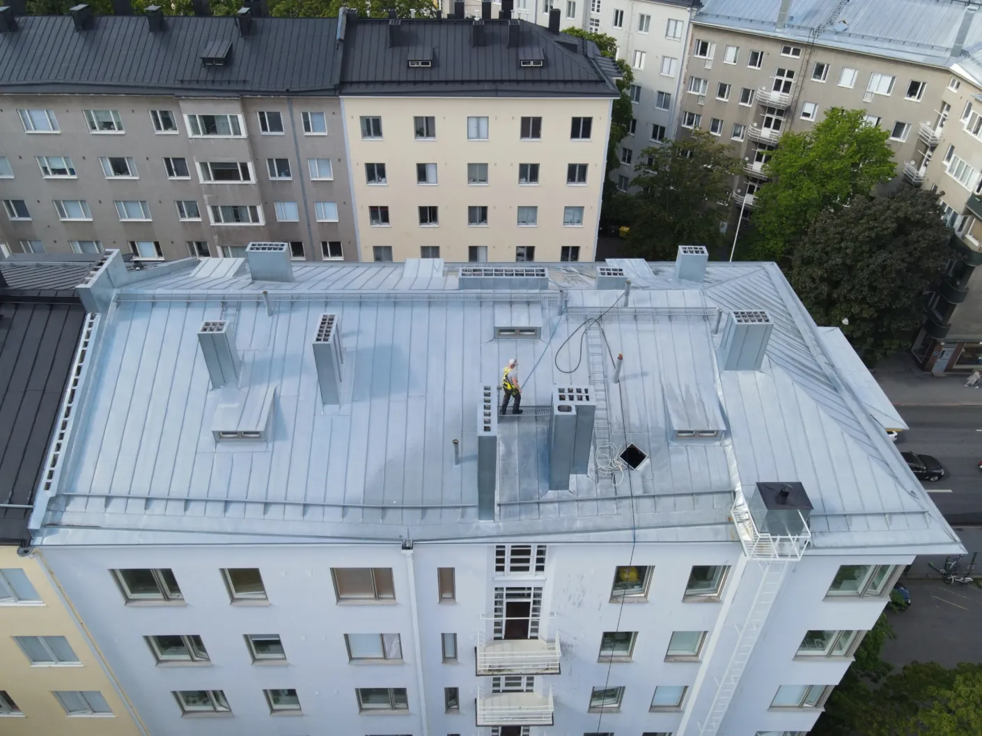 Korterelamu plekk-katus enne puhastust, kulunud helehall pind, tehnik katuseharjal linnakvartalis