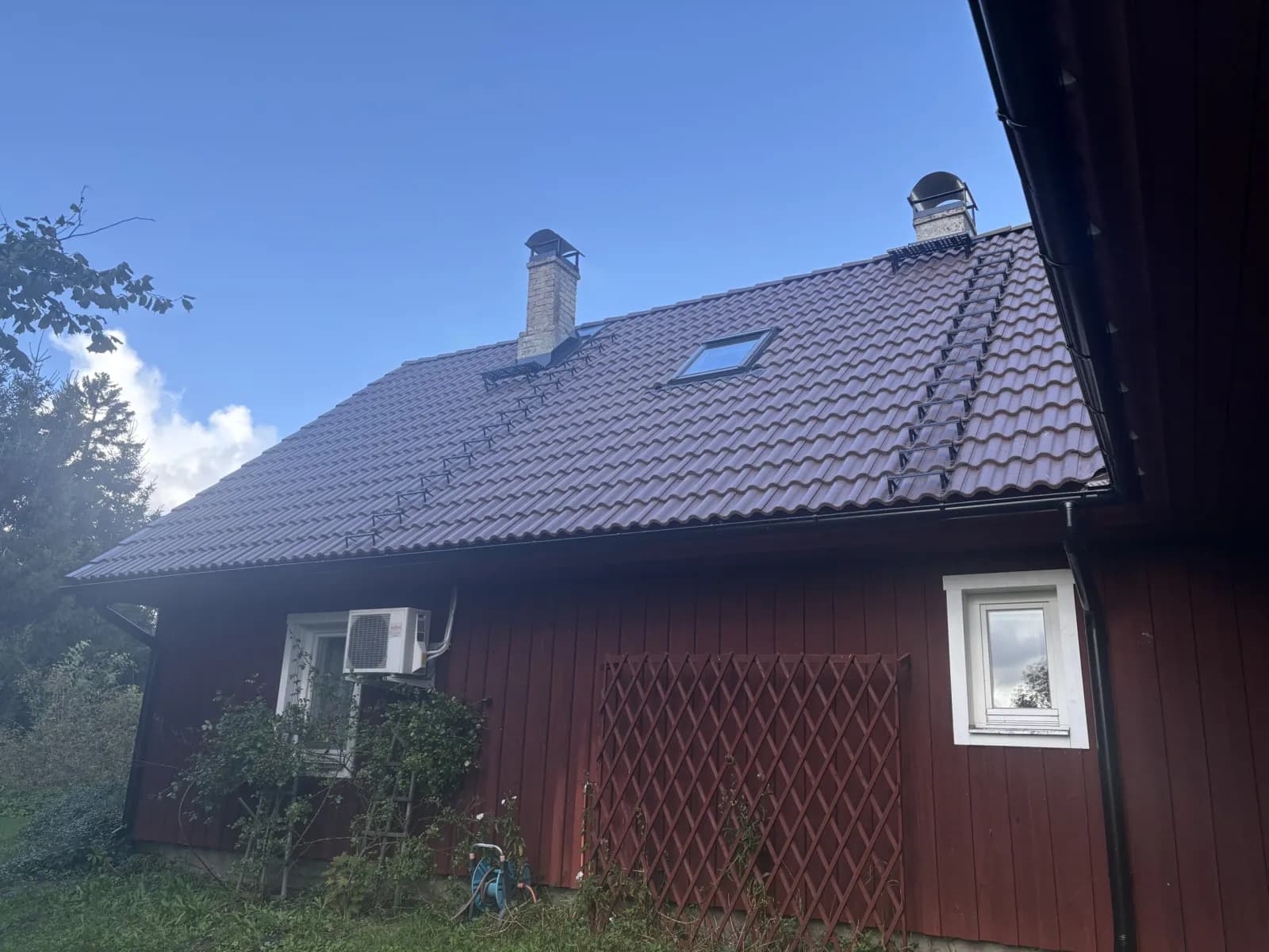 Tumepunane puitmaja pruuni viilkatuse ja katuseaknaga
