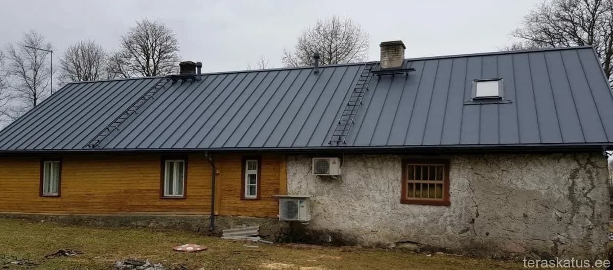 Puitmaja tumehalli valtsplekk-katusega, katuseredelid mõlemal katusepoolel ja soojuspumbad seinal